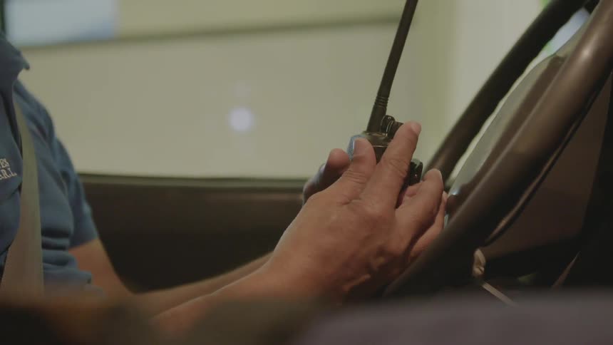 A paramedic sits in a vehicle holding a walkie talkie