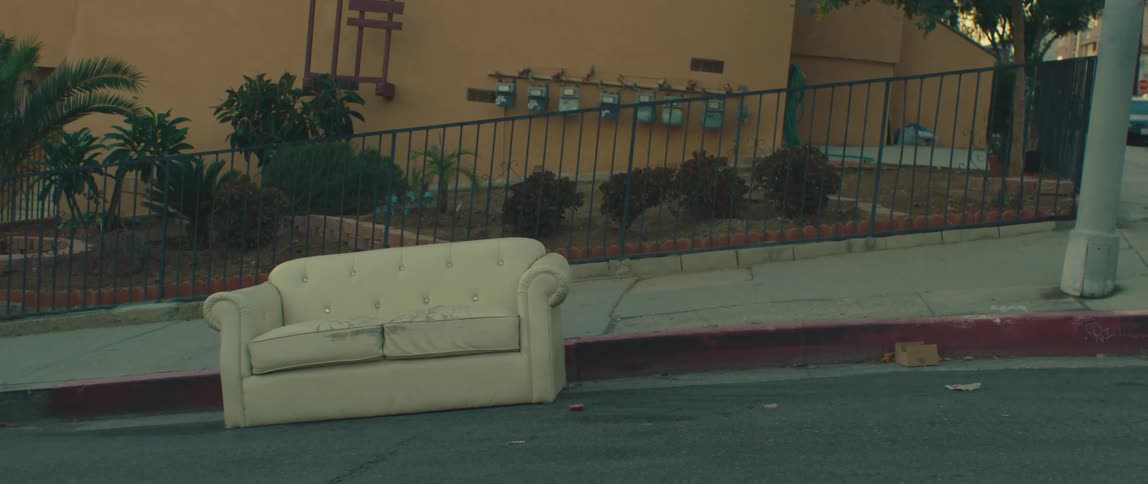 A worn sofa sits abandoned on a street curb in a suburban neighborhood