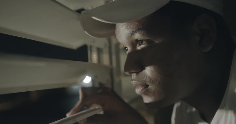 A man wearing a white hat looks through window blinds