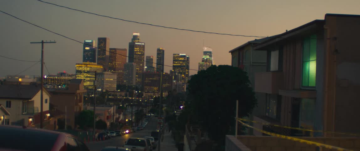 Downtown los angeles glows at dusk as city lights illuminate the skyline beyond a quiet residential street