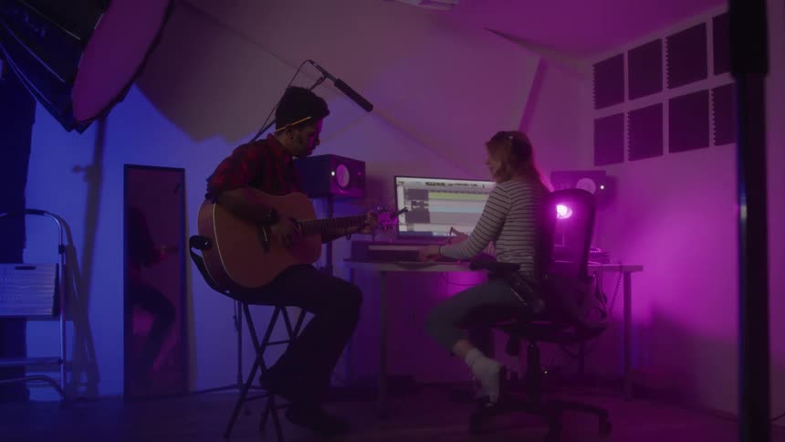 Two musicians collaborate in a dimly lit recording studio