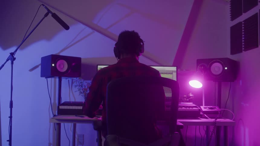 A music producer in a studio creates music wearing headphones and working behind a computer