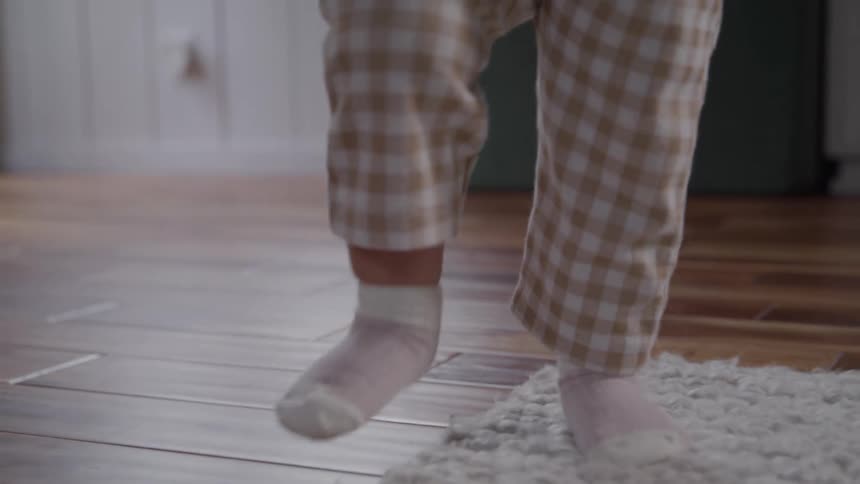 A toddler with pigtails holds an adults hand while walking indoors looking down with focus