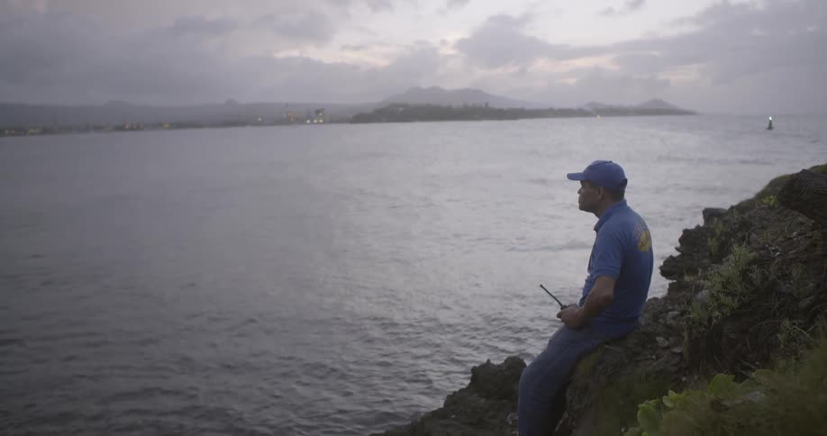 A man leans against rocks on the shoreline