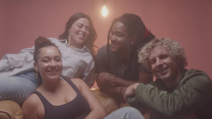 A group of four young adults smile and laugh as they sit together and pose