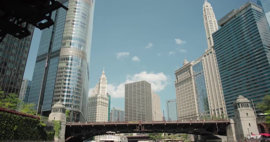 Skyscrapers line the chicago river with the wrigley building and tribune tower prominent viewed from beneath a raised bridge