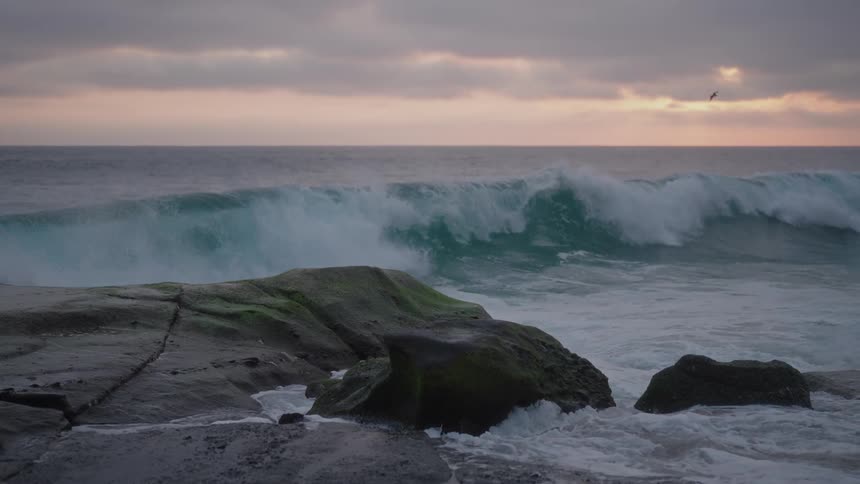 Waves hit rocky shores as birds fly at sunset