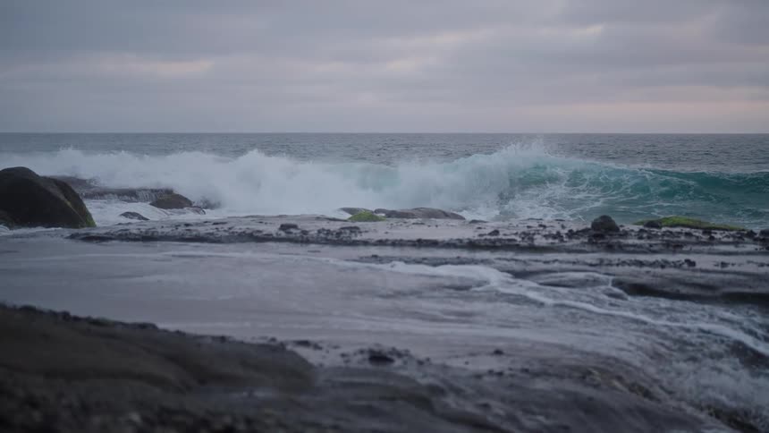 A powerful wave crashing against a rocky shoreline creating a dramatic explosion of foam and spray