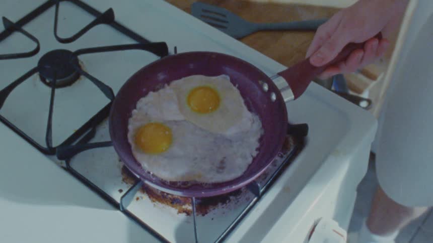 Man fries two eggs on a gas burner in his kitchen