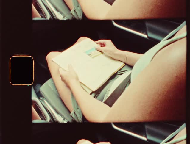 A woman in a sleeveless dress reads a book while sitting in a seat