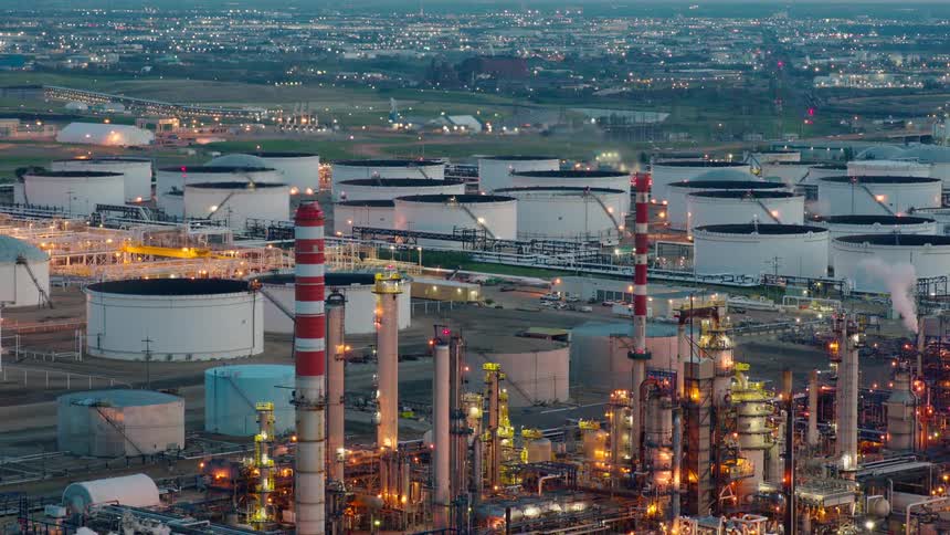 An aerial view shows a large refinery illuminated with lights with many white petroleum storage tanks