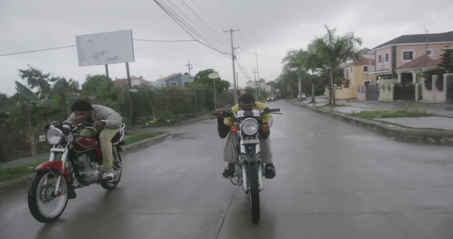Two men ride motorcycles in the rain