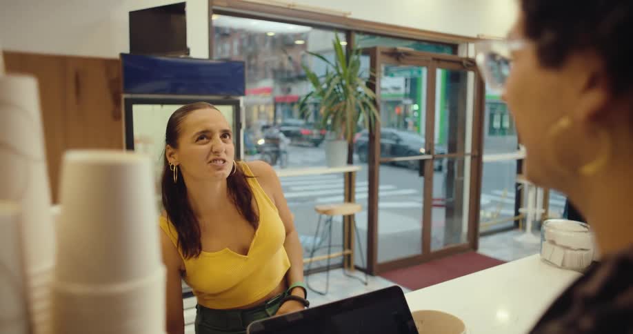 A young woman with a dog is smiling at someone across a counter in a shop the woman is wearing a yellow top and the shop has large windows and a glass door