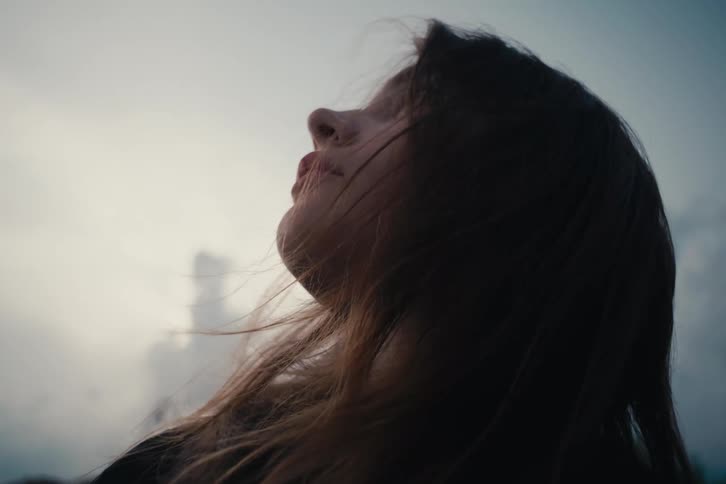 Closeup of a woman face with hair blowing against a cloudy sky