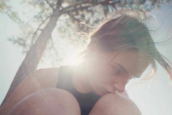 Young woman with a pensive expression rests her face on her knee under sunlight