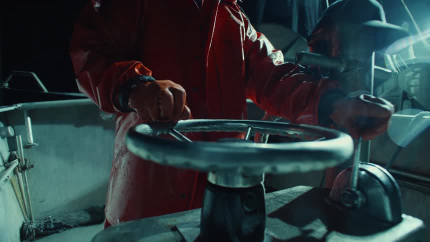 Person wearing a red raincoat and gloves steers a boat at night
