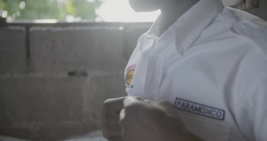 A black man buttons up his paramedic uniform