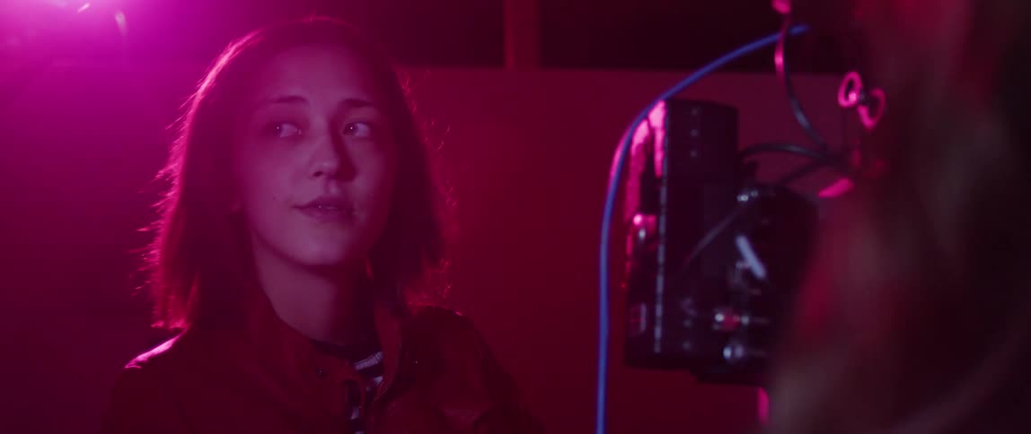 A woman operates film equipment under dramatic pink lighting