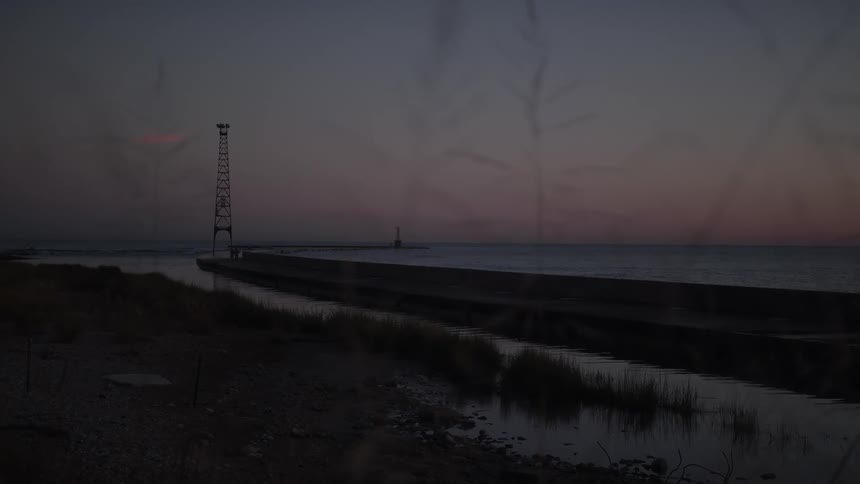 A coastal pier with a tall metal tower stands by the ocean at dusk