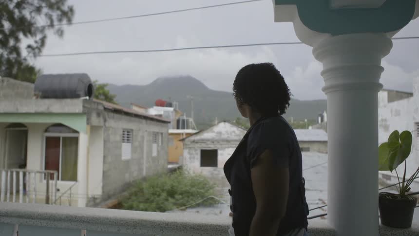 A woman stands on a balcony and stares into the distance
