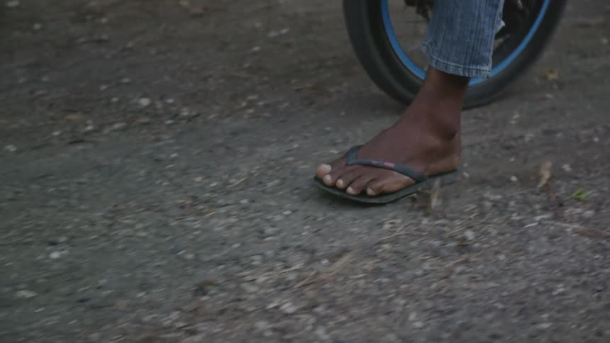 A man in flip flops rides a motorcycle and slides his foot on the ground