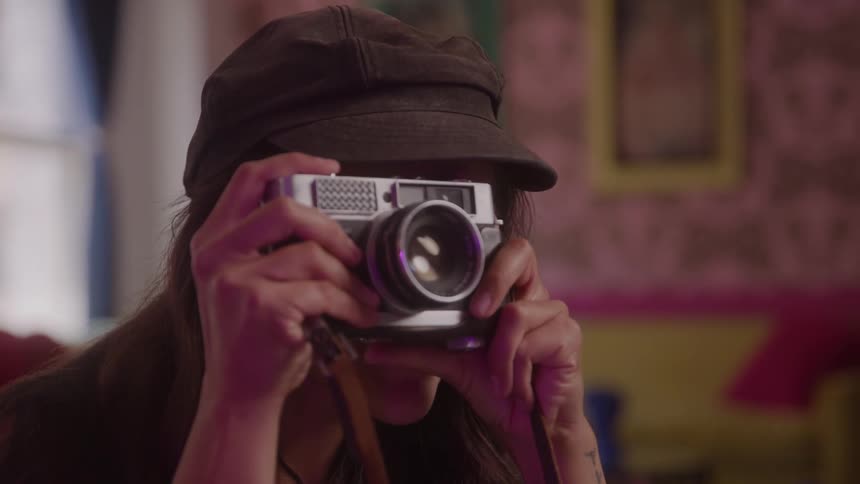 A smiling woman holds up a vintage camera and takes pictures in a colorful room