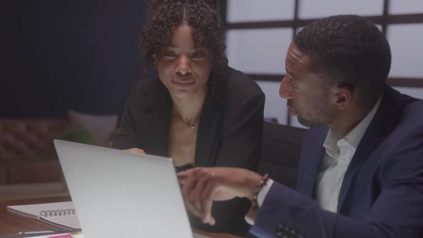 Coworkers sitting at a table reference a computer during a discussion