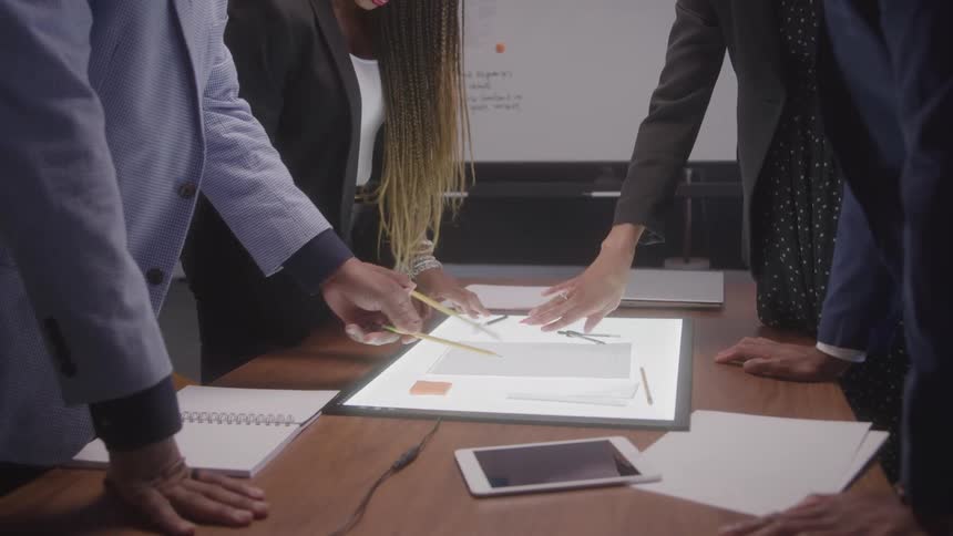 People gathered around a lit table pointing at documents and discussing project details