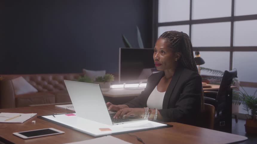 Woman working on a laptop at a lit desk in a modern office setting