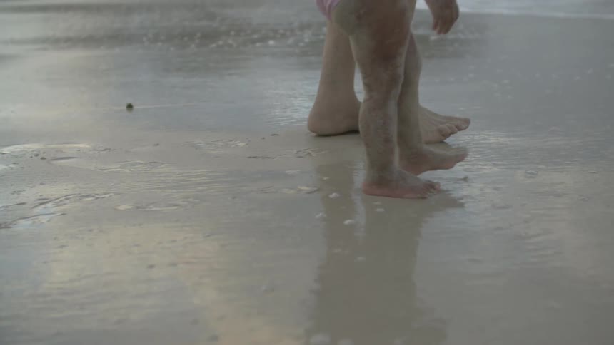 A man and toddler's feet are shown walking on a sandy beach