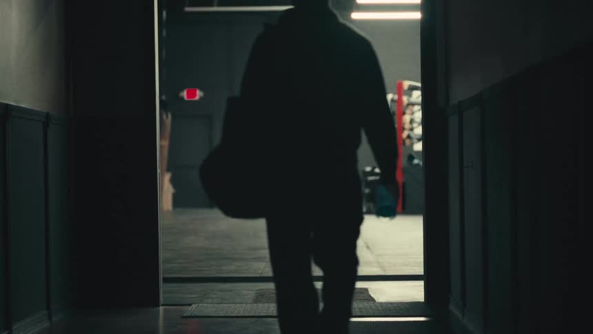 Silhouette of a person walking through a hallway towards a lit space
