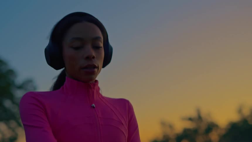 Close up of a young black woman checking her smart watch before continuing to jog across a field outdoors at sunset