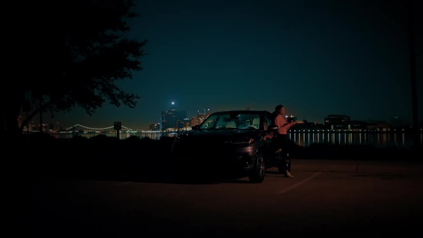 A young black woman steps out of her car parked outdoors at night and wears her headphones before jogging away