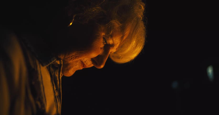Older woman concentrates on a task in an area lit by candlelight at night