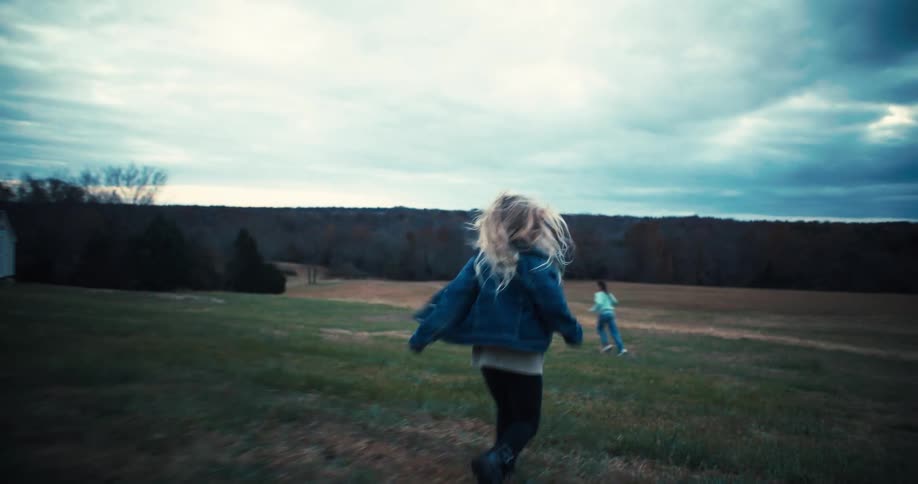 Two girls running after a dog in an open field