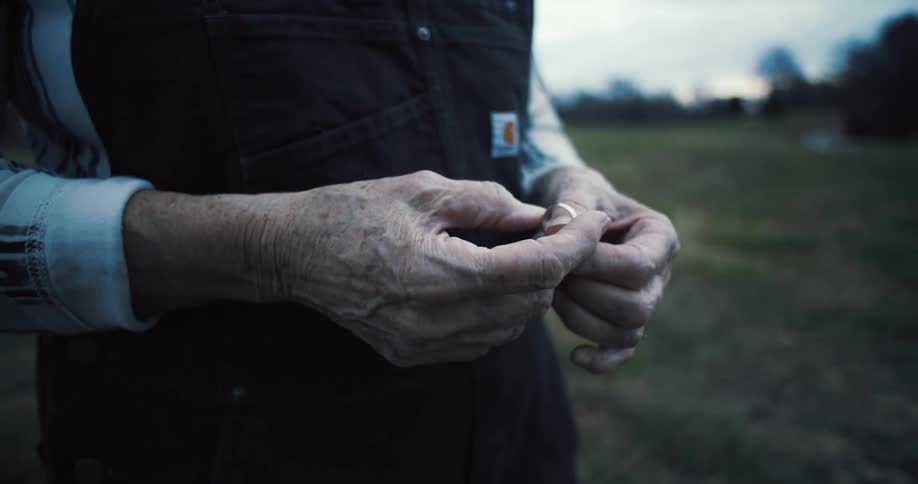 Aged hands holding ring in field