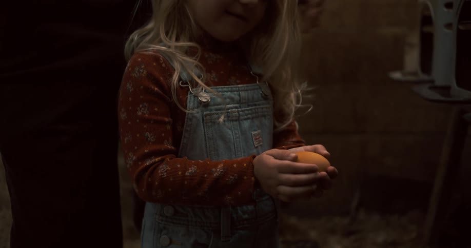 A girl is handing a large egg in the coop