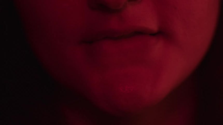 A close view shows a persons mouth and chin with their lips moving slightly as a dark red light illuminates the lower part of their face