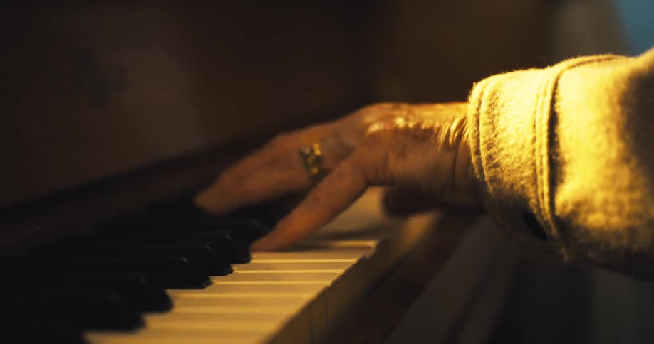 An elderly person hands play the piano keys