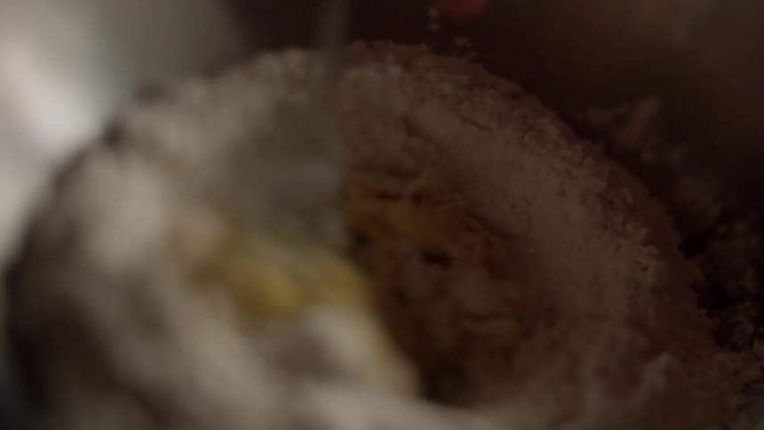 A person stirs an egg into a flour mixture