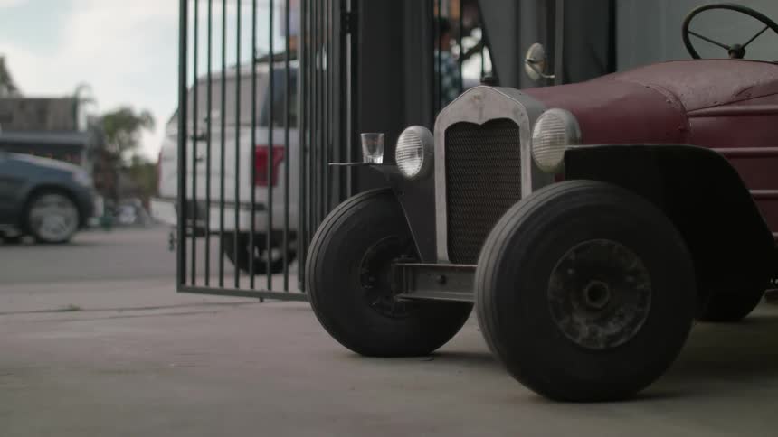 Pedestrians walk near an antique car in a city setting