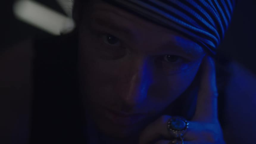 Man tinted blue by colored lighting stares while touching his face