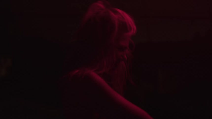 The video shows a woman with blonde hair in a dark room illuminated by a red light she is seen moving her head from side to side and appears to be dancing