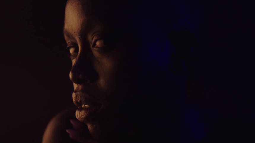 A young woman sits inside a dark room at night
