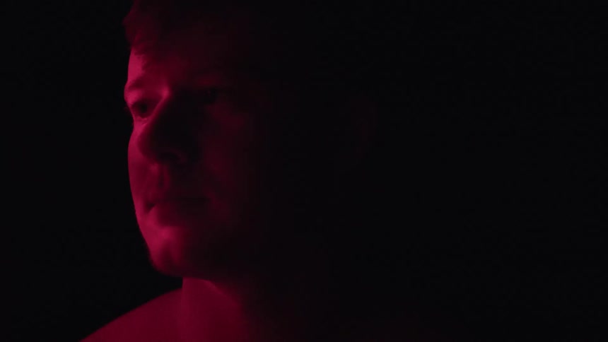 A lowangle closeup shot of a mans face in the dark is shown the mans face is illuminated with a red light