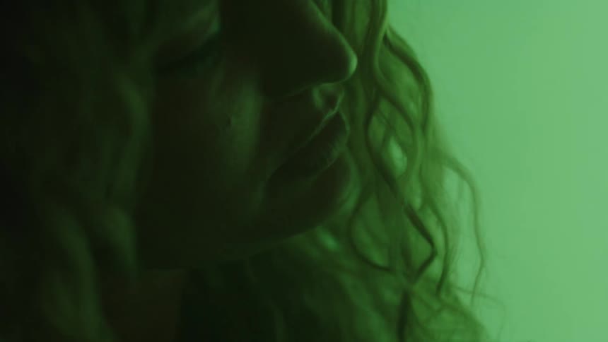 Face in profile partially shadowed under soft green lighting