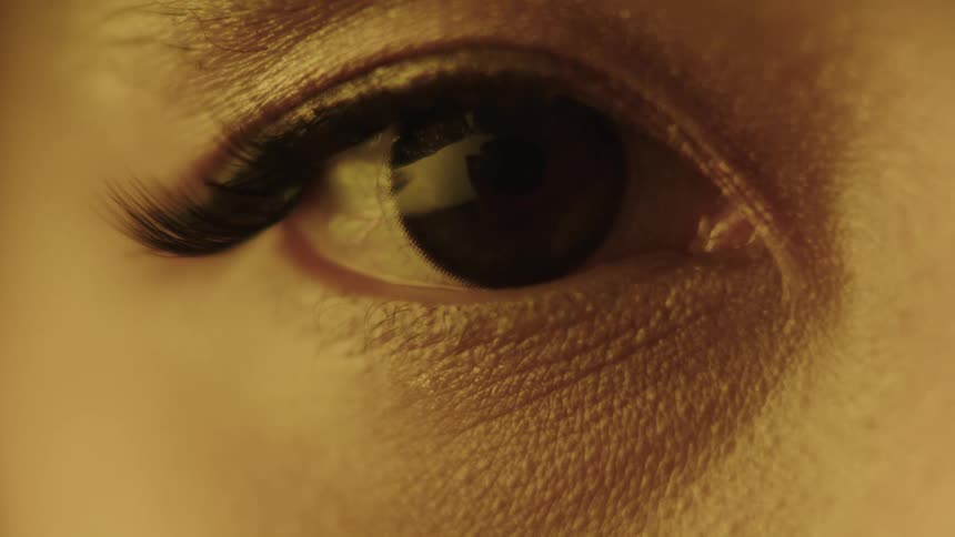 A persons eye blinks in an extreme closeup shot with the texture of the skin and eyelashes visible