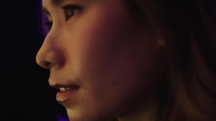 A profile shot of a womans face is shown her face is illuminated by different colored lights including green and purple
