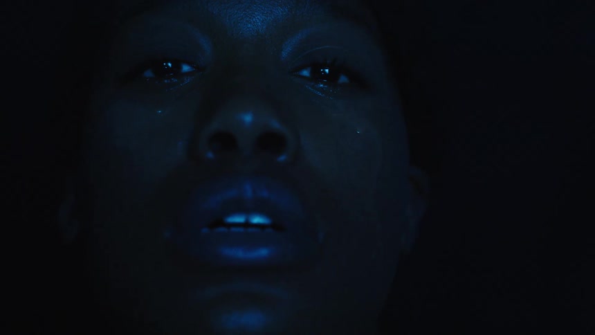 A closeup of a womans face shows a teardrop under blue light