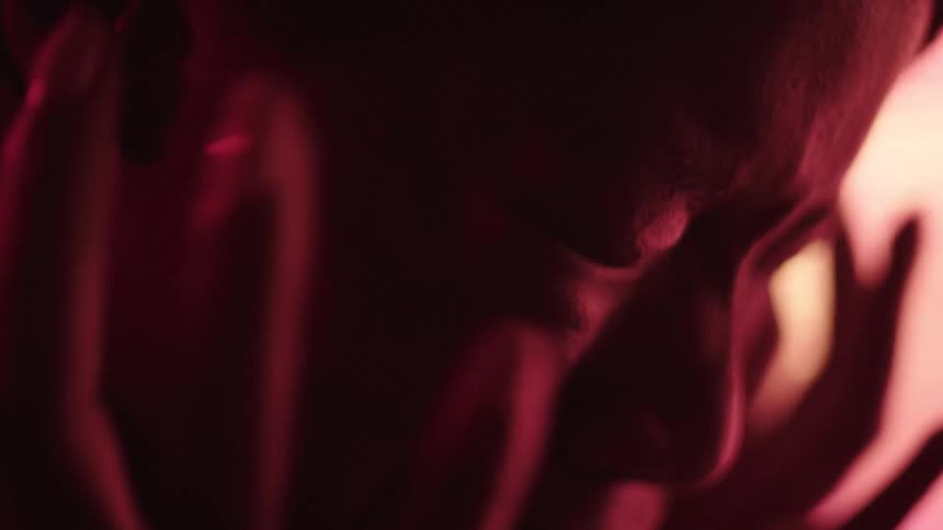 Face covered by hands under red and blue lighting
